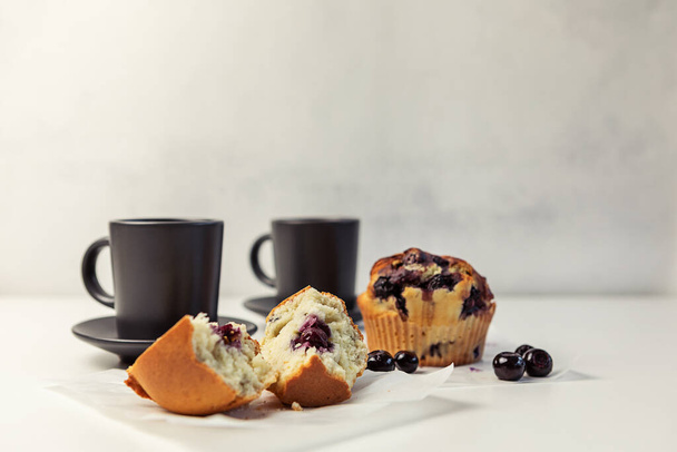 Вкусные черничные кексы и черника на белом столе, темные чашки кофе. селективный фокус - Фото, изображение