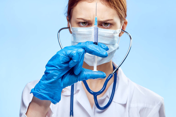 doctor woman in blue gloves with stethoscope nurse with glasses injection syringe laboratory light background - Foto, afbeelding