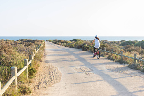 Woman riding a bike on a sunny day. You can see the sea in the background. Relaxed sport concept. - Foto, Imagen