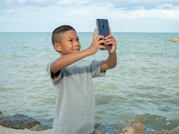 A boy using a phone to take a selfie on a sea background - Photo, Image