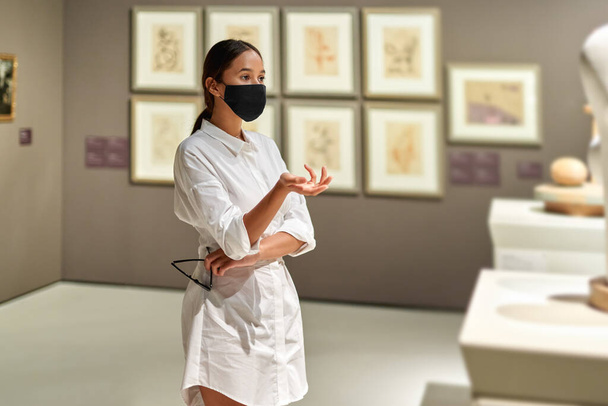 Kobieta odwiedzający w masce antywirusowej w muzeum historycznym patrząc na zdjęcia. - Zdjęcie, obraz