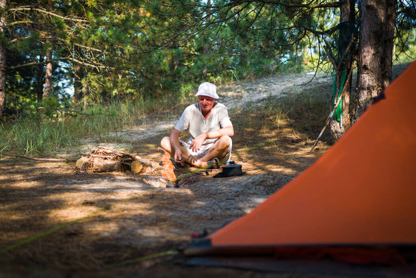 Man looks at a bonfire near a tent in a pine forest - Foto, Bild