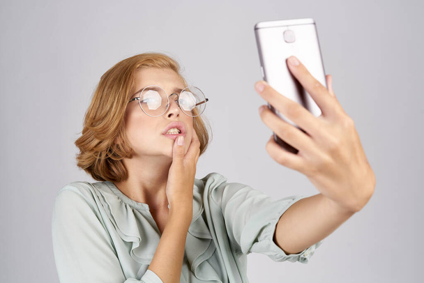 женщины с мобильным телефоном в руках фотографируют себя в рубашке на светлом фоне - Фото, изображение