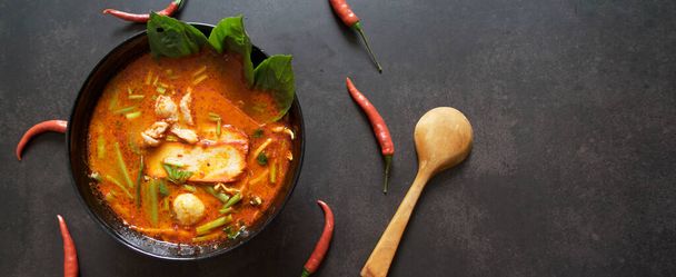 Πανοραμικό πανό για το διαδίκτυο, ταϊλανδέζικο φόντο τροφίμων. Πιάτα της Ταϊλάνδης κουζίνα. Tom γιαμ χοιρινή σούπα σε μαύρο πιάτο, ρύζι σε ξύλινο πιάτο στο τραπέζι σκούρο φόντο, χώρος για κείμενο στα δεξιά - Φωτογραφία, εικόνα