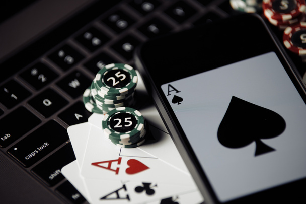 Poker play online concept. Close-up poker chips, playing cards and smartphone on keyboard - Photo, Image