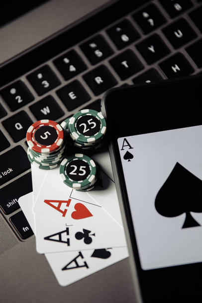 Online poker casino theme. Gambling chips, smartphone and playing cards on keyboard close-up - Photo, Image