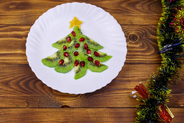 Kivi dilimleri ve nar ağacından yapılmış Noel ağacı ve ahşap masa üzerindeki Noel süsü. Üst Manzara. Noel ve Yeni Yıl bayramı tatlıları için yaratıcı bir fikir. Çocuklar için komik yemek fikri. - Fotoğraf, Görsel