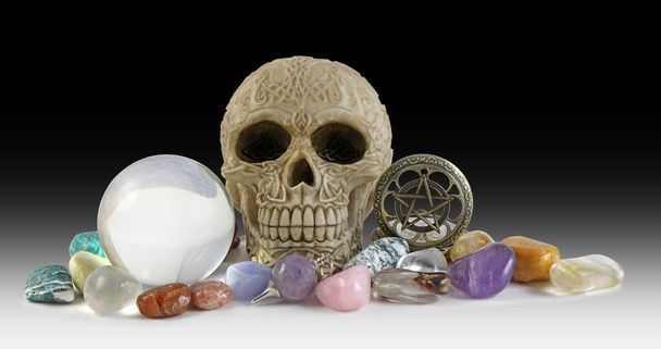 Cristales y cráneo Wiccan Fondo oscuro: bola de cristal, cráneo celta, reloj de bolsillo pentáculo y selección de cristales de curación caídos sobre un fondo negro con espacio para copiar - Foto, imagen