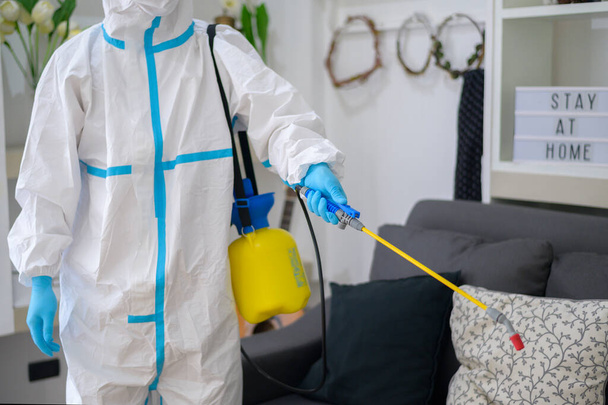 A medical staff in PPE suit is using disinfectant spray in living room, Covid-19 protection , disinfection concept . - Фото, зображення