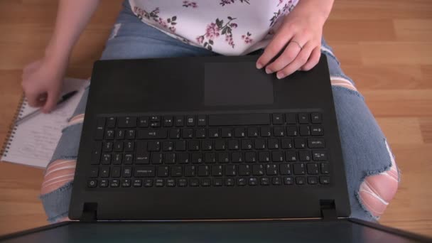 Een persoon zit gekruiste benen op een houten vloer terwijl hij typt op zijn laptop - Video