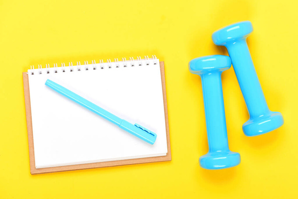 Notebook, pen and gym equipment top view on yellow background - Foto, Imagem
