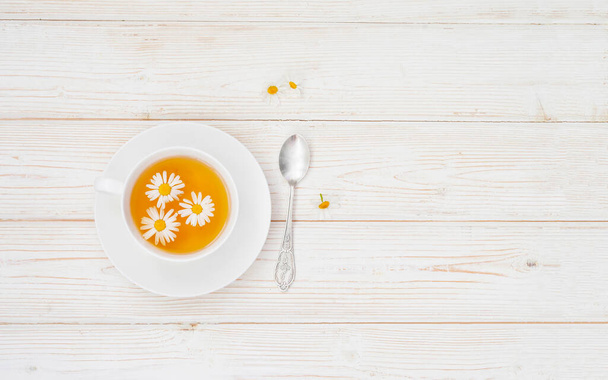 Cup of herbal tea with honey and chamomile flowers on the white wooden background. Natural organic alternative medicine concept flat layout - Photo, image