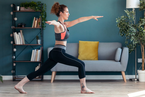 Shot of attractive sporty young woman doing hypopressive exercises in living room at home. - Photo, image