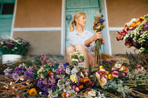 Gedroogde bloemen liggen op de grond op de achtergrond van een vrouwelijke bloemist het creëren van een compositie. Wazig. Achtergrond. Vakantie boeketten creëren als een bedrijf. - Foto, afbeelding