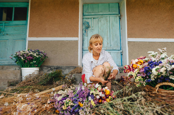 Bella donna adulta decoratore crea una composizione di fiori secchi. Fiorista fa mazzi di fiori secchi in campagna. - Foto, immagini