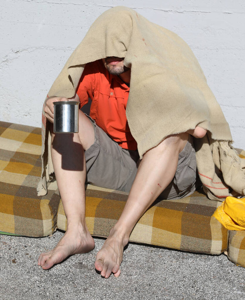 oud dakloze alcoholist smeekt om aalmoezen op een smerig matras zonder schoenen - Foto, afbeelding