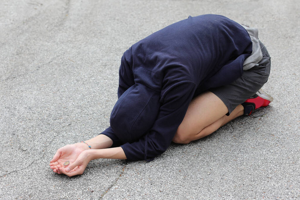 joven gitano agachado en el suelo pide limosna para comer - Foto, Imagen