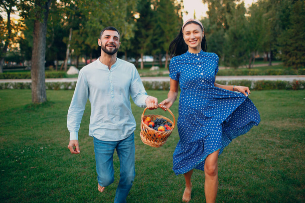 Счастливая пара с фруктами в корзине для пикника в парке. - Фото, изображение
