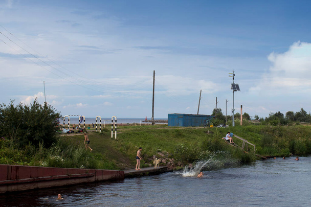 BELOZERSK, Oroszország - 2020. augusztus 3., Belozersk város rakpartja. Vologda régió. A fiúk úsznak egy csatornában a tó közelében. - Fotó, kép
