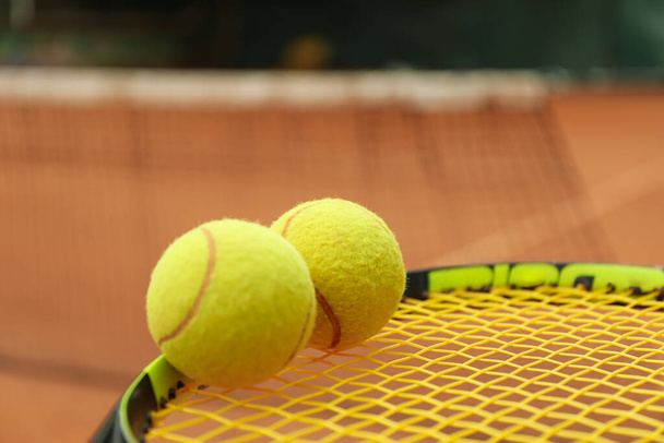 Tennisracket met tennisballen tegen kleiveld - Foto, afbeelding