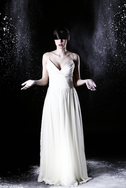 Beautiful girl in white dress and flying dust over black background - Photo, Image