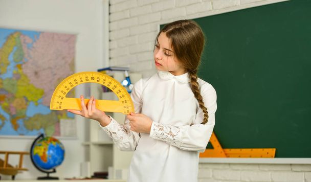 Cute little schoolgirl with geometrical tool for mathematics. Elementary school mathematics or maths. Mathematics matters. Small child holding ruler for mathematics lesson. Science and Technology - Foto, imagen