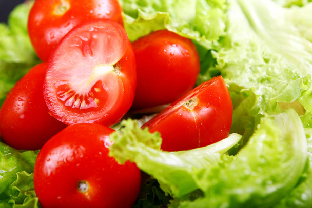 Fresh and wet tomatoes lying on the salad leaves - Photo, Image