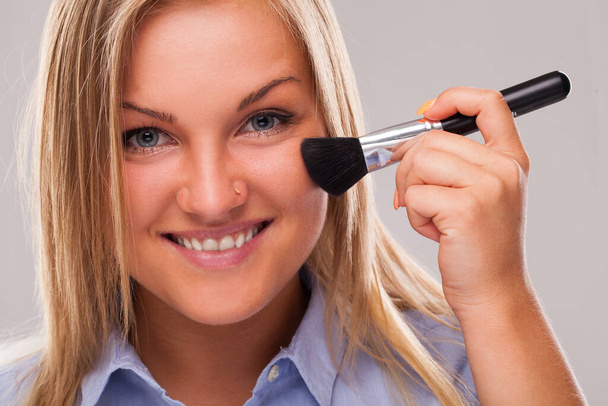 Closeup portrait of young blond caucasian woman smiling with cosmetic brush - Photo, Image