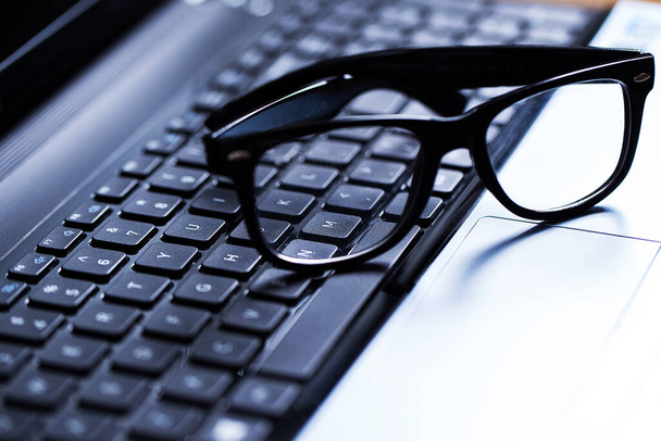 Closeup picture of a glossy laptop keyboard with glasses above it - Zdjęcie, obraz