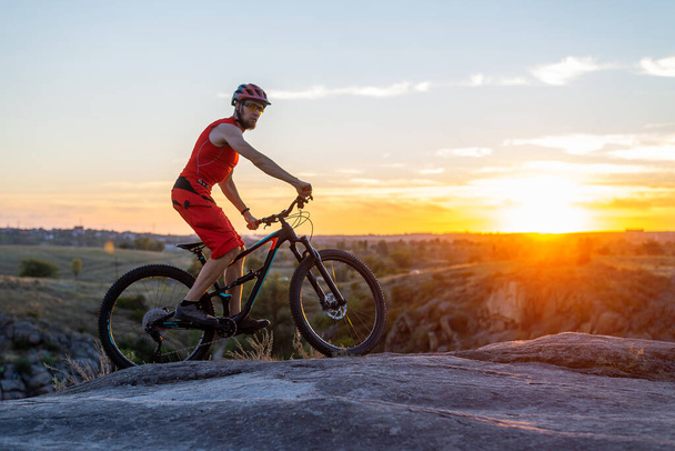 The cyclist rides on the rocks on a mountain bike, in the background of a sunset, a copy of the free space. Active lifestyle, cycling. MTB. - Fotografie, Obrázek