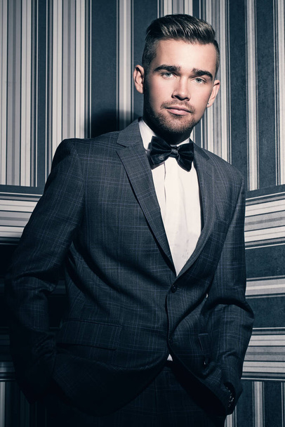Egy öltönyös és nyakkendős jóképű férfi portréja, aki csíkos háttérrel pózol. - Fotó, kép