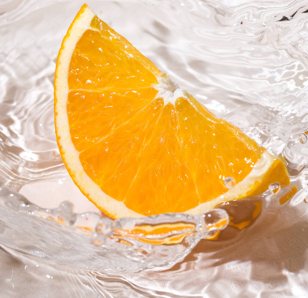 Kawałek pomarańczy wpada do wody. - Zdjęcie, obraz