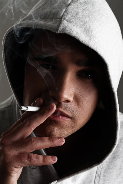 Молодой и красивый мужчина в капюшоне курит сигарету
 - Фото, изображение