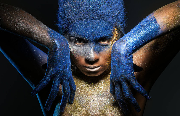 Πορτραίτο μιας γυναίκας που θέτουν που καλύπτονται με μπλε και χρυσό χρώμα - Φωτογραφία, εικόνα