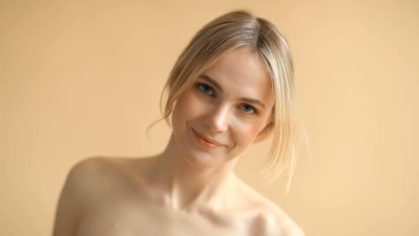 Retrato de mujer joven natural con el pelo rubio posando en la cámara sobre fondo beige  - Metraje, vídeo