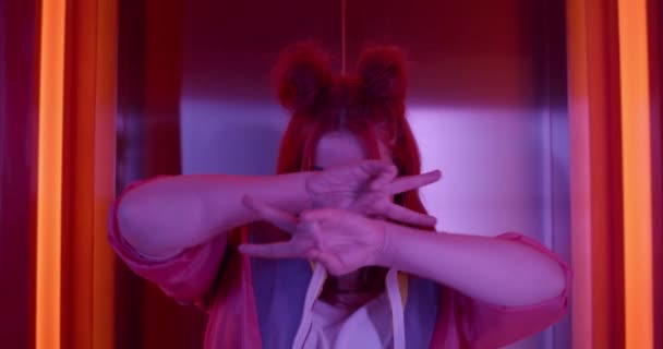 Crop view of happy young woman in trendy sports suit dancing and looking to camera. Beautiful female clubber with stylish hairdo laughing andfunny moving g near elevator in neon lights. - Metraje, vídeo