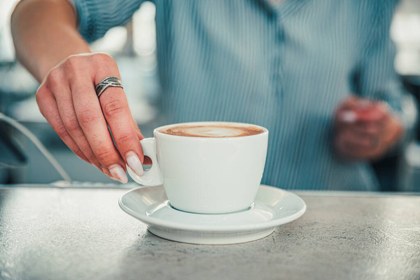 Closeup female barista hands holding cup of aromatic latte or cappuccino coffee in bar or cafe - Foto, immagini