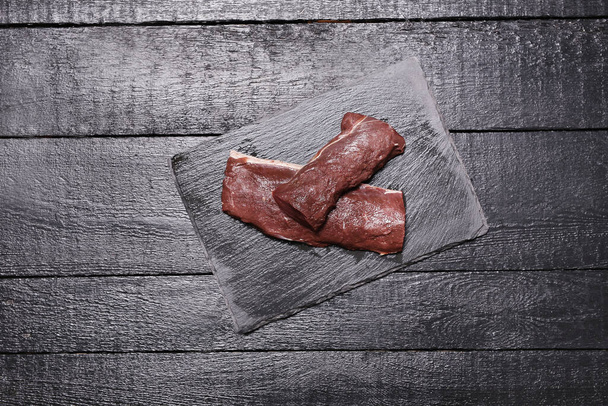 Νωπό κρέας σε μαύρο ξύλο κοπής - Φωτογραφία, εικόνα