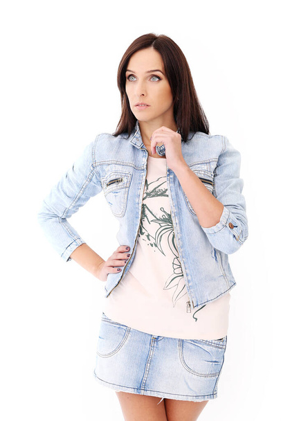 Portrait of a beautiful brunette in jeans jacket and skirt who is posing over a white background - Fotoğraf, Görsel