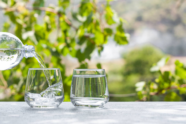 Fersh, clean, drink water pouring in to glass from a plastic bottle. Select focus blurred nature background. Healthy lifestyle, water balance control, skin care concept. - Photo, Image