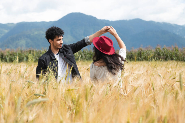 Молода пара танцює в центрі поля пшениці - іспаномовне подружжя веселиться на заході сонця - молодий чоловік крутить свою подругу за руку. - Фото, зображення