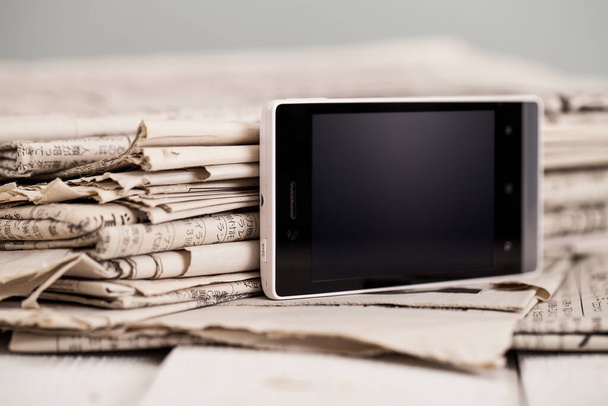 Pilha de jornais em preto e branco com um smartphone preto em uma mesa de madeira - Foto, Imagem