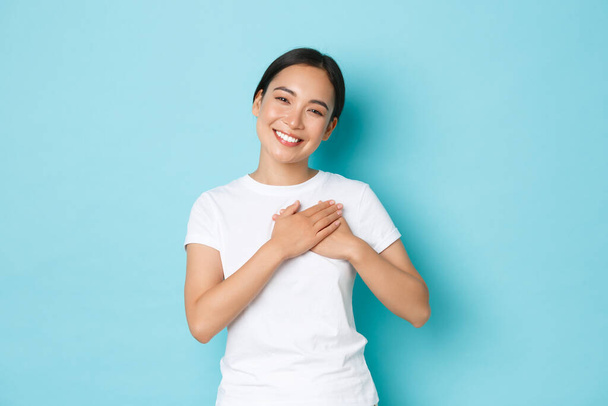 Lifestyle, beauty and shopping concept. Portrait of touched and grateful pretty asian girl thanking for flattering compliment, holding hands on heart and smiling with caring, tender expression - Photo, Image
