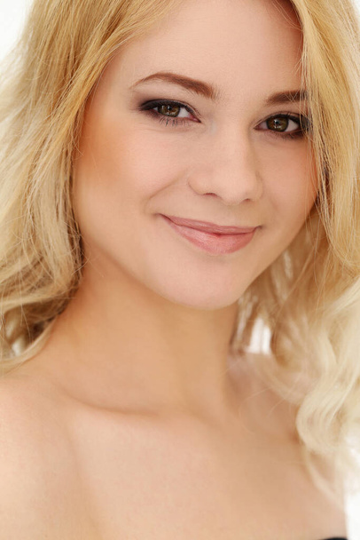 Portrait d'une belle fille blonde aux cheveux bouclés qui pose sur un fond blanc - Photo, image