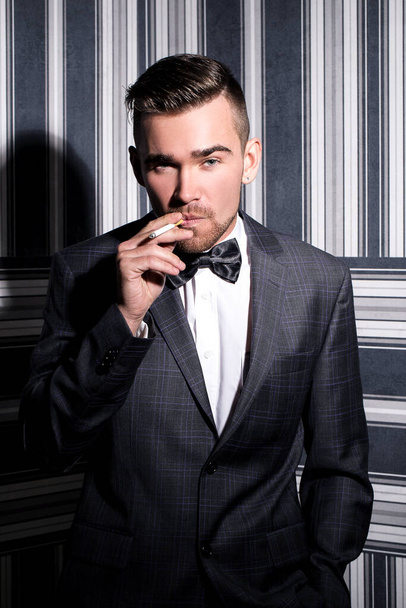 Handsome man with a beard who is wearing a dark suit and a tie is posing over a striped background - Foto, Imagem
