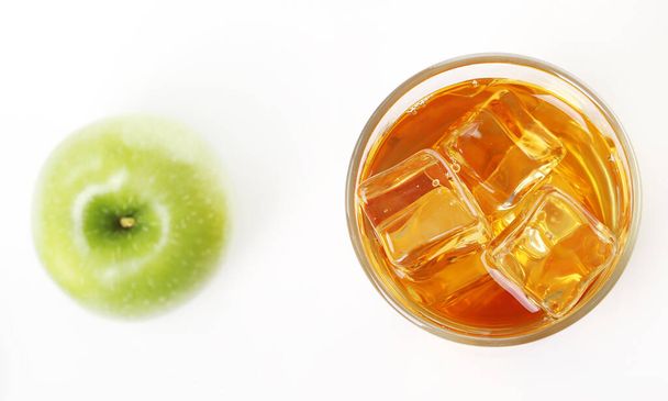 Стакан освежающего яблочного сока с большим количеством льда внутри и зеленое яблоко возле стакана - Фото, изображение
