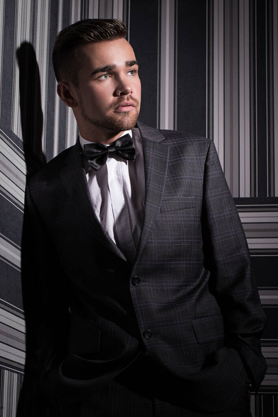 Porträt eines gutaussehenden Mannes in Anzug und Krawatte, der über einem gestreiften Hintergrund posiert - Foto, Bild