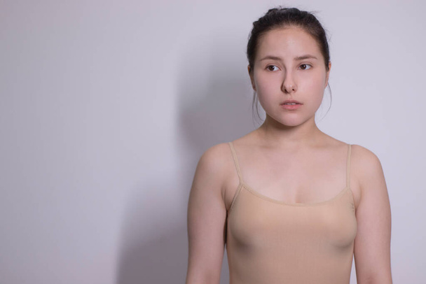 Emotionales Porträt der attraktiven Brünetten, Schauspielerin im beigen Unterhemd - Body auf weißem Hintergrund. Raum für Text - Foto, Bild