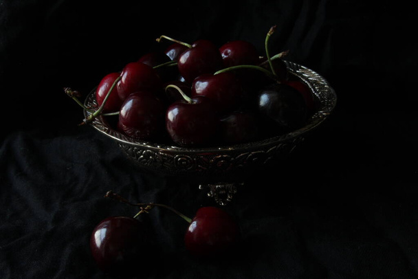 Fresh sweet ripe cherries on rustic plate on black background. Close up. - Foto, Imagem