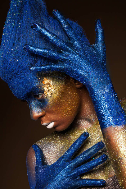 Portrait of a woman who is posing covered with blue and gold paint - Photo, Image